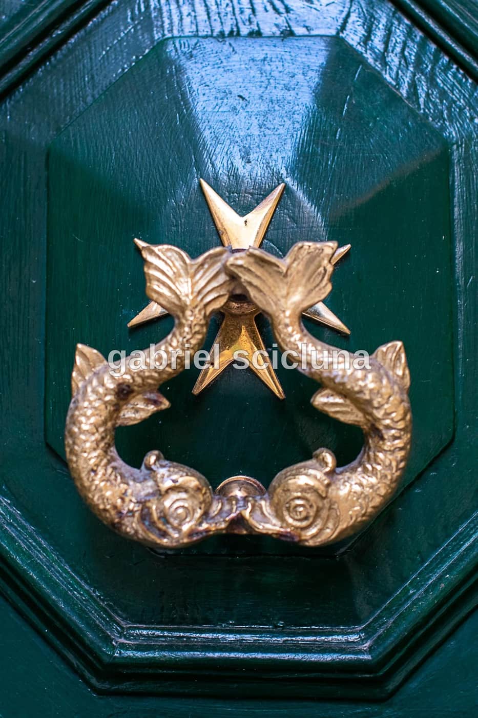An ornate traditional Maltese door knocker set against a green doorway.