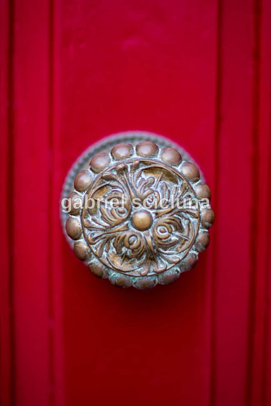 A traditional silver-coloured Maltese door knocker mounted on a vibrant red door.