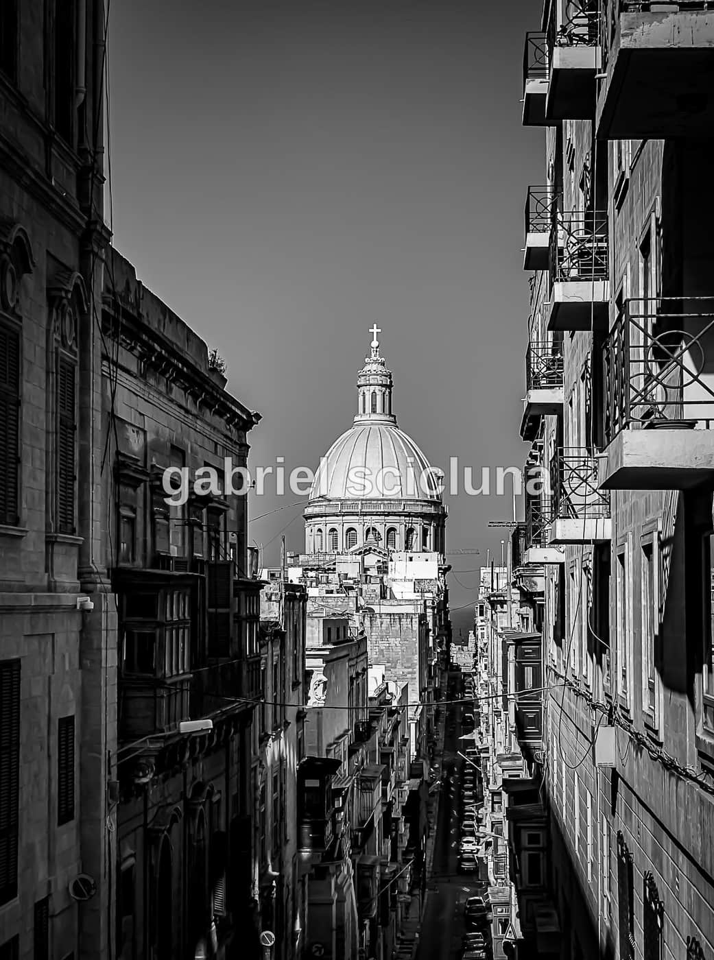 A black-and-white photograph of Valletta's streets and historic stone architecture.